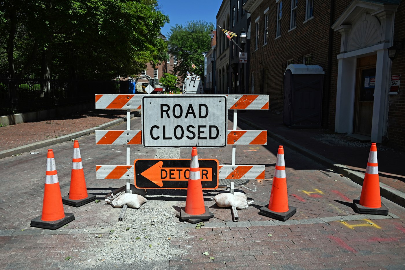 A road closure barrier with cones and a detour arrow
