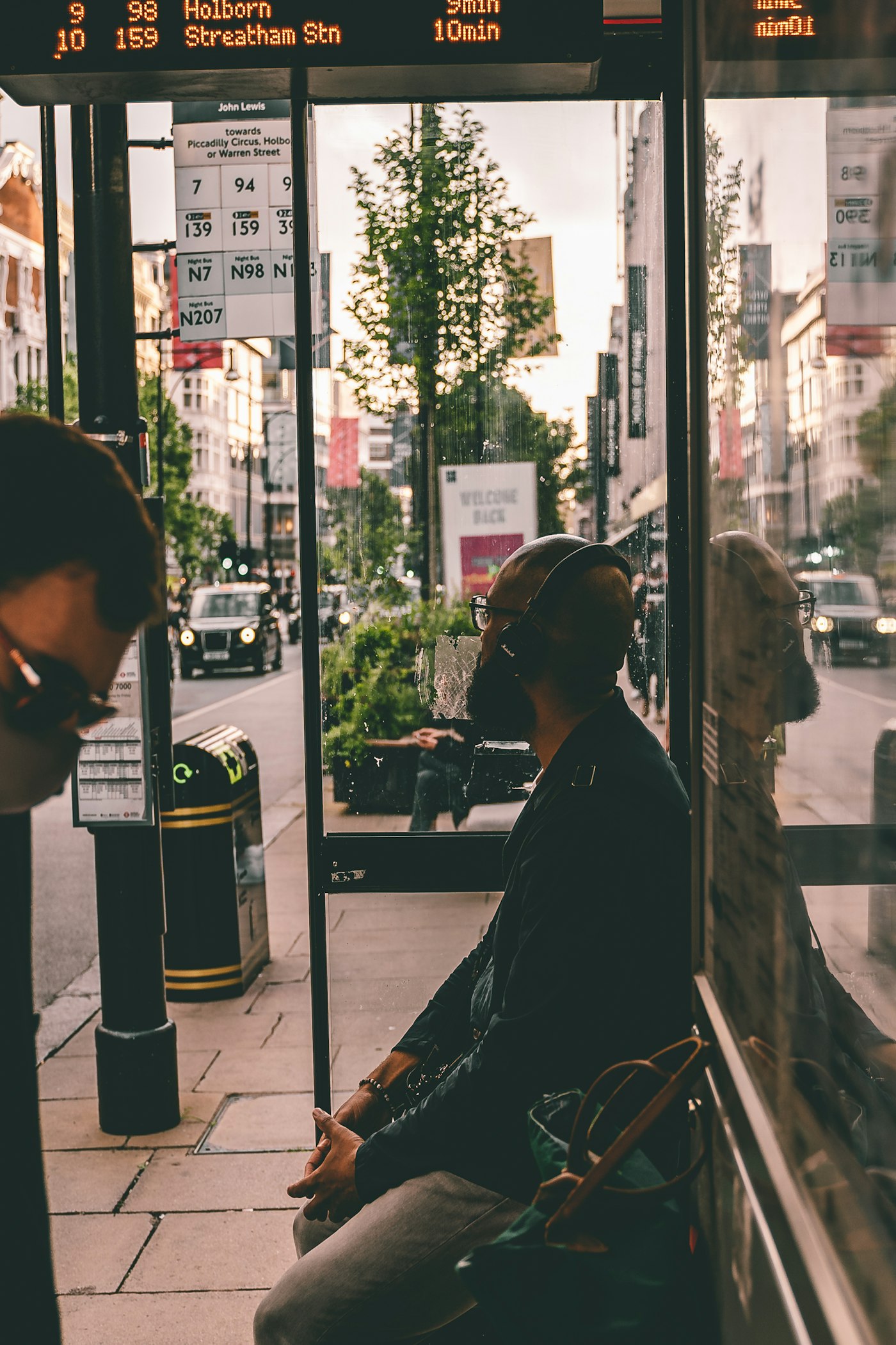 A passenger seated inside a glass bus shelter